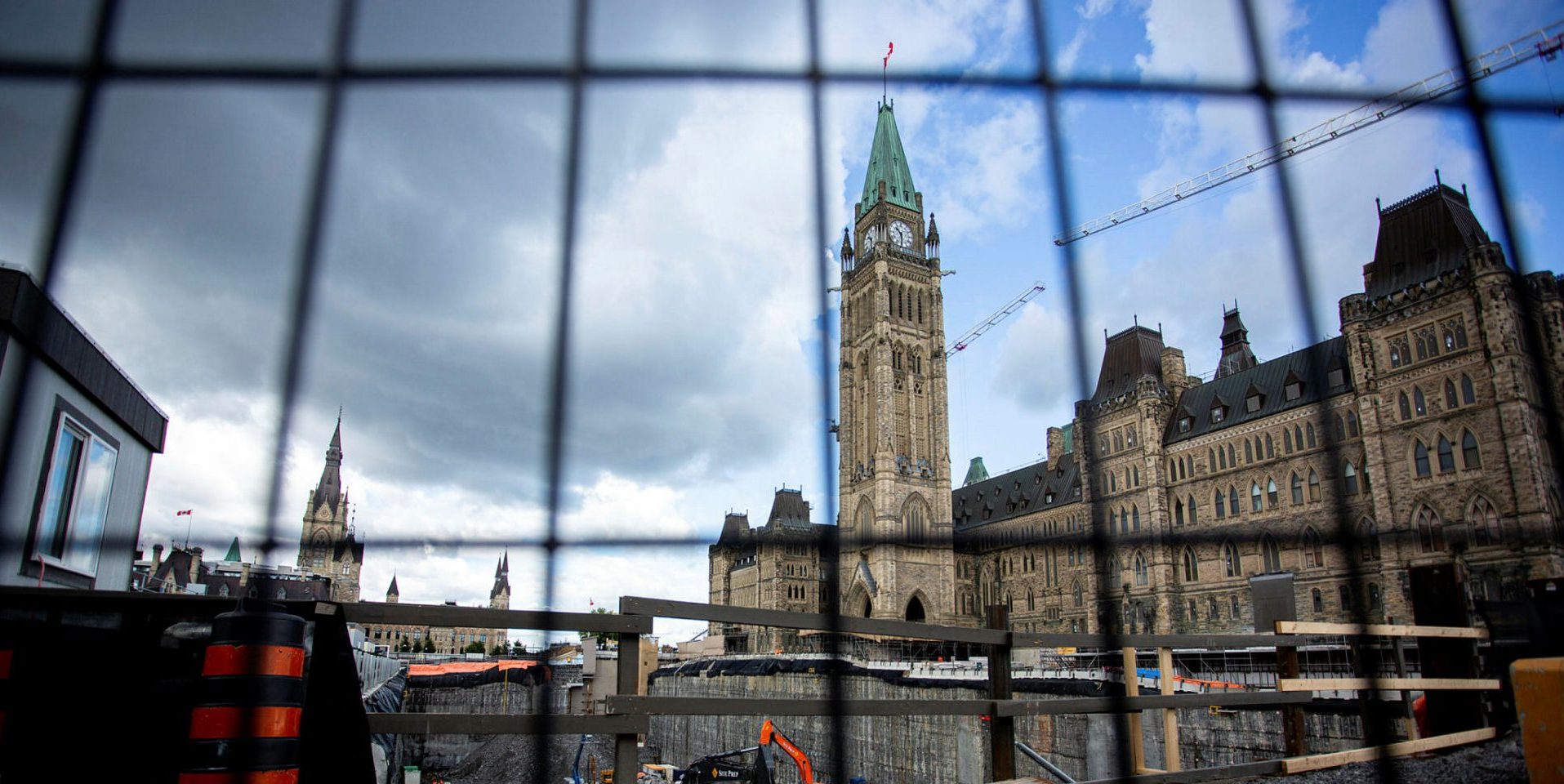 The Peace Tower is pictured behind a construction fence and pit on July 12, 2022, that has been excavated during the Centre Block revitalization project. The Hill Times photograph by Andrew Meade