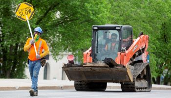 A construction worker escorts a loader down the road in front of West Block on May 25, 2020.